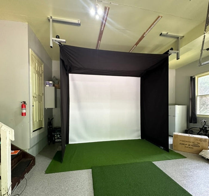 Indoor golf simulator setup with a screen and green mat on a gray floor.