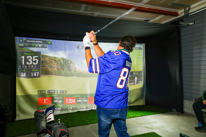 Man swinging in Vanish 16H retractable golf simulator enclosure