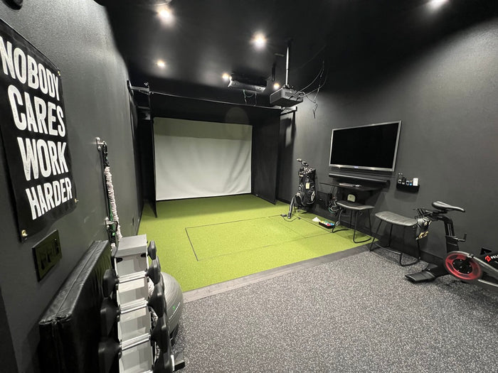 Golf simulator and gaming room with a TV, gaming equipment, and motivational poster on a gray wall.