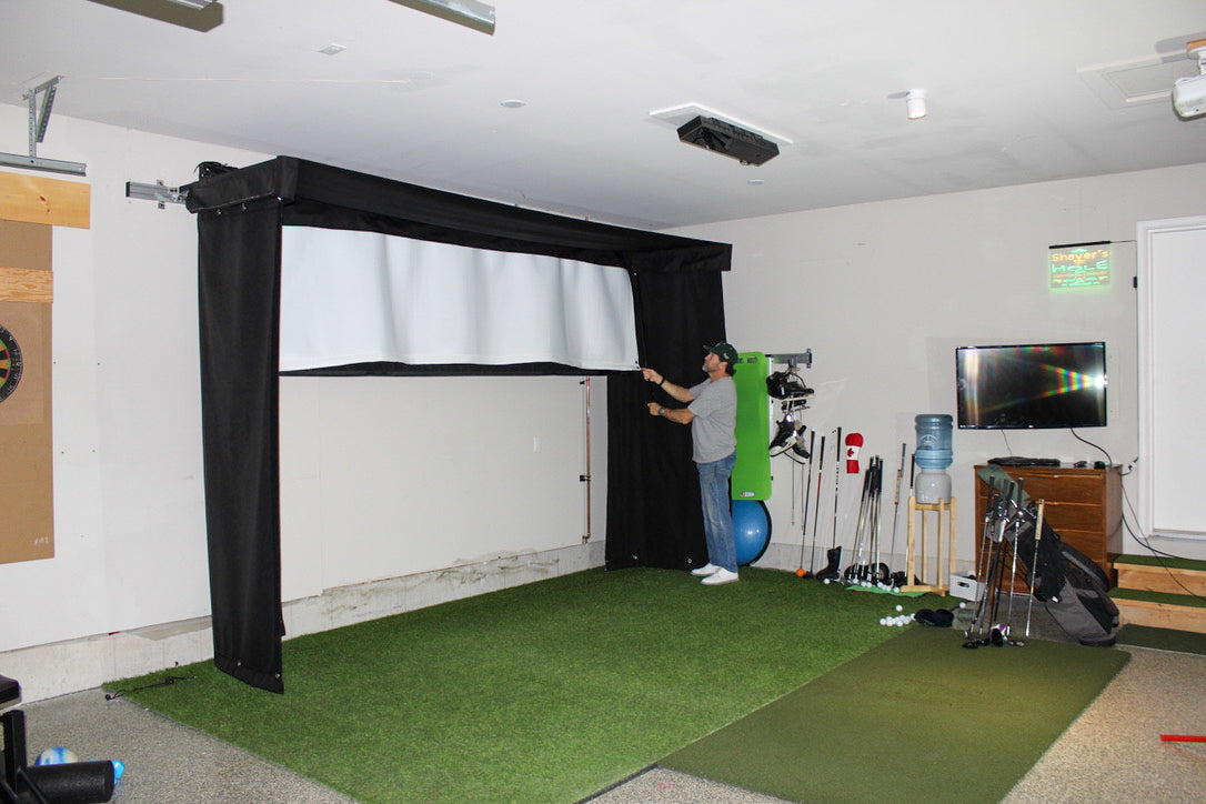 Indoor golf simulator setup in a home garage with a person using it.